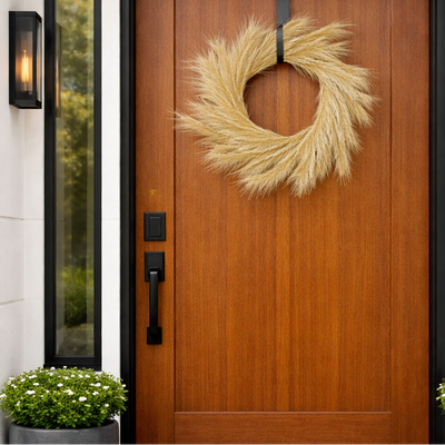 Wooden door with a decorative wreath, potted plant, and wall sconce.