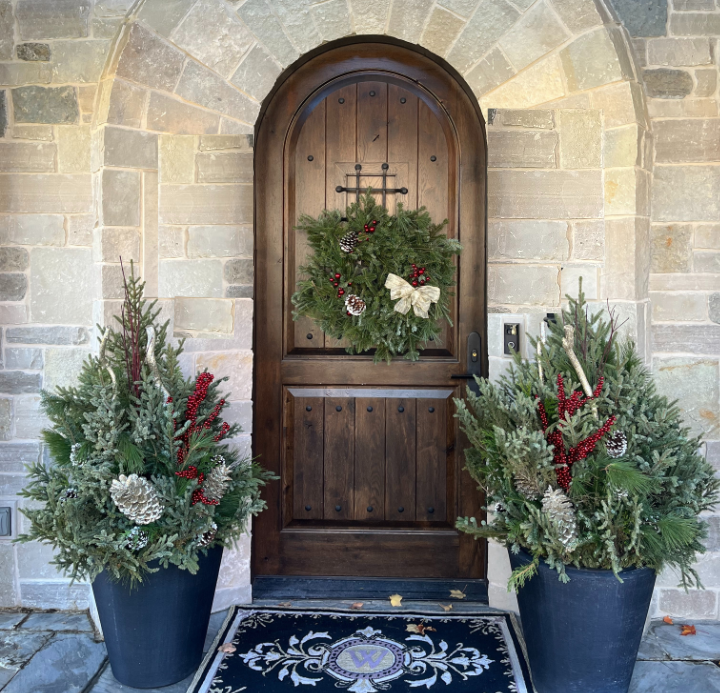 Winter season planters on porch with wreath hanging on wood door